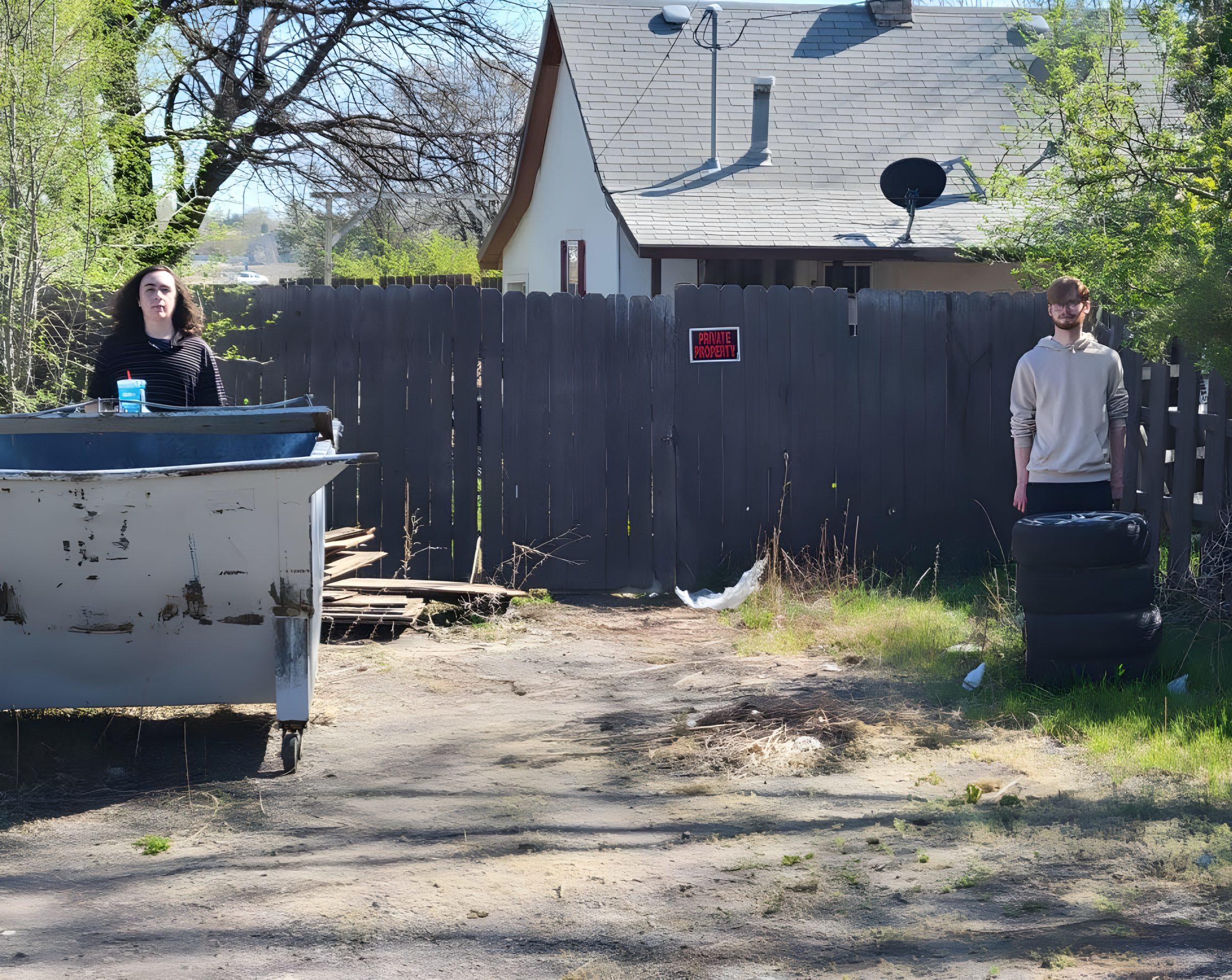 Gabe and Christien standing behind a dumpster and tires